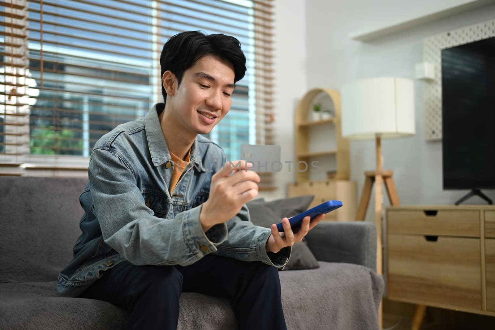 Handsome asian man holding a credit card and purchasing online on smartphone.
