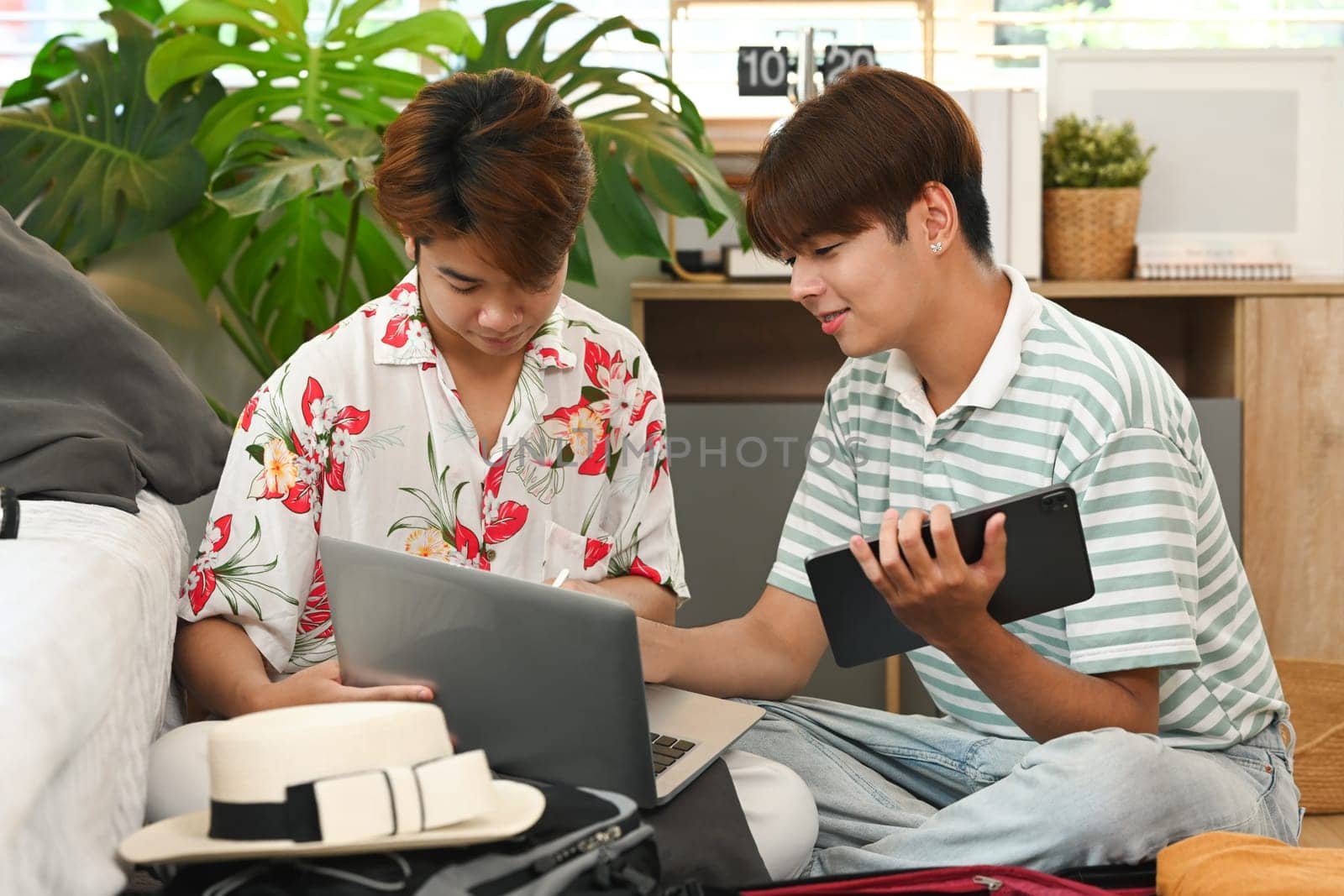 Happy gay couple preparing luggage for travel trip and booking hotel reservation on laptop.