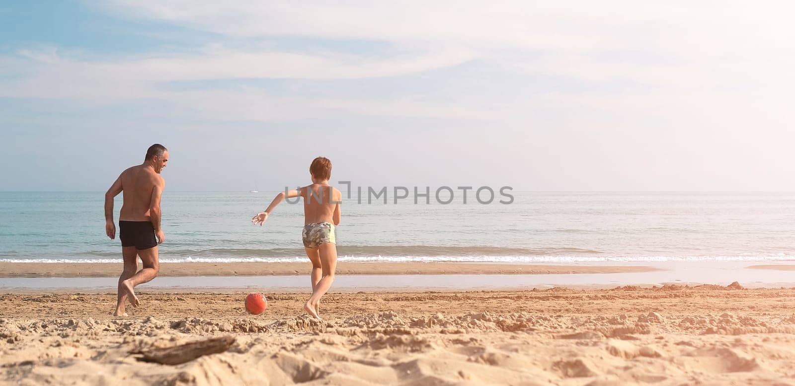 Father and son running on the beach with copy space. Playful casual family enjoying