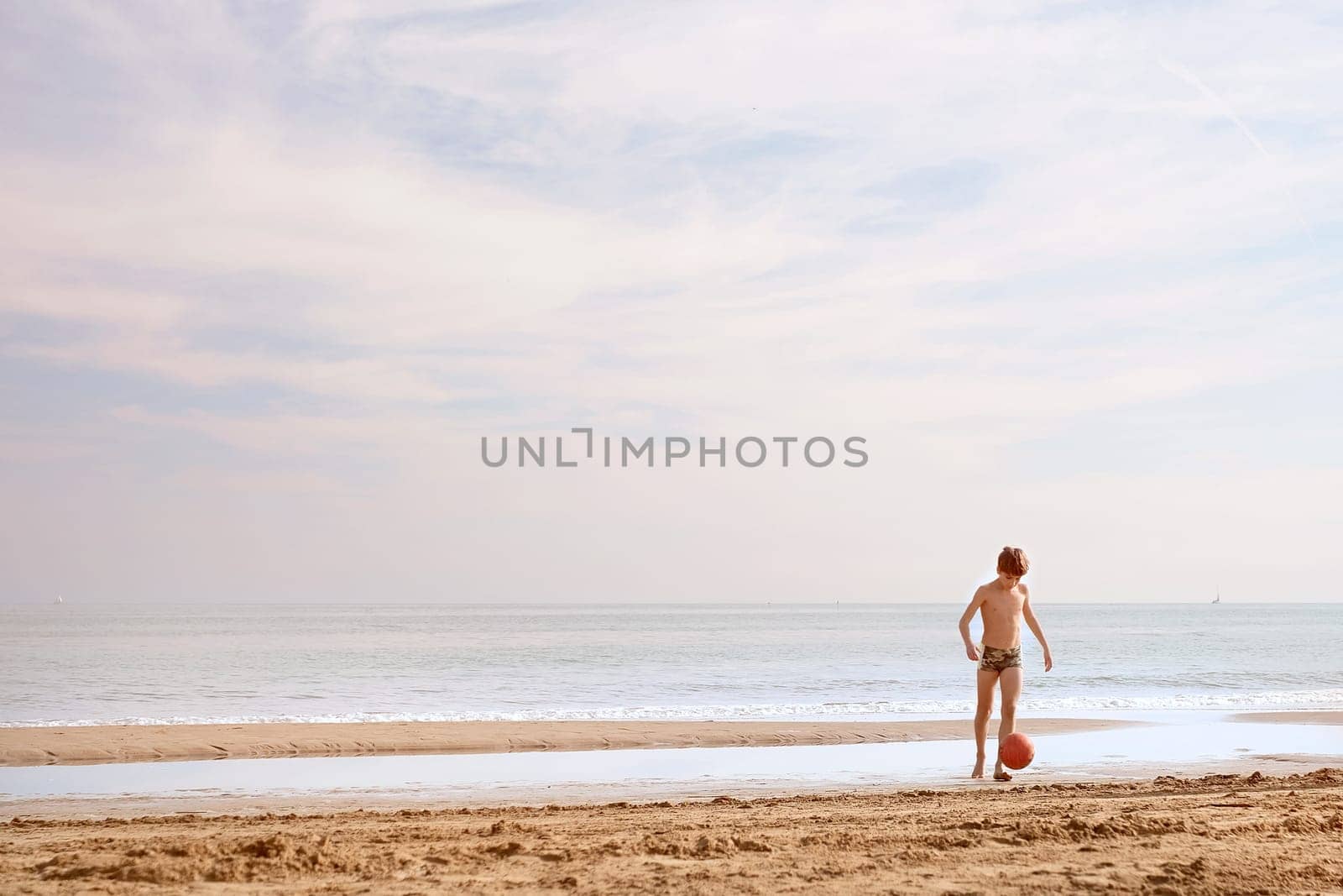 Boy is playing with ball on the beach with copy space. Playful casual family enjoying. Summer concept