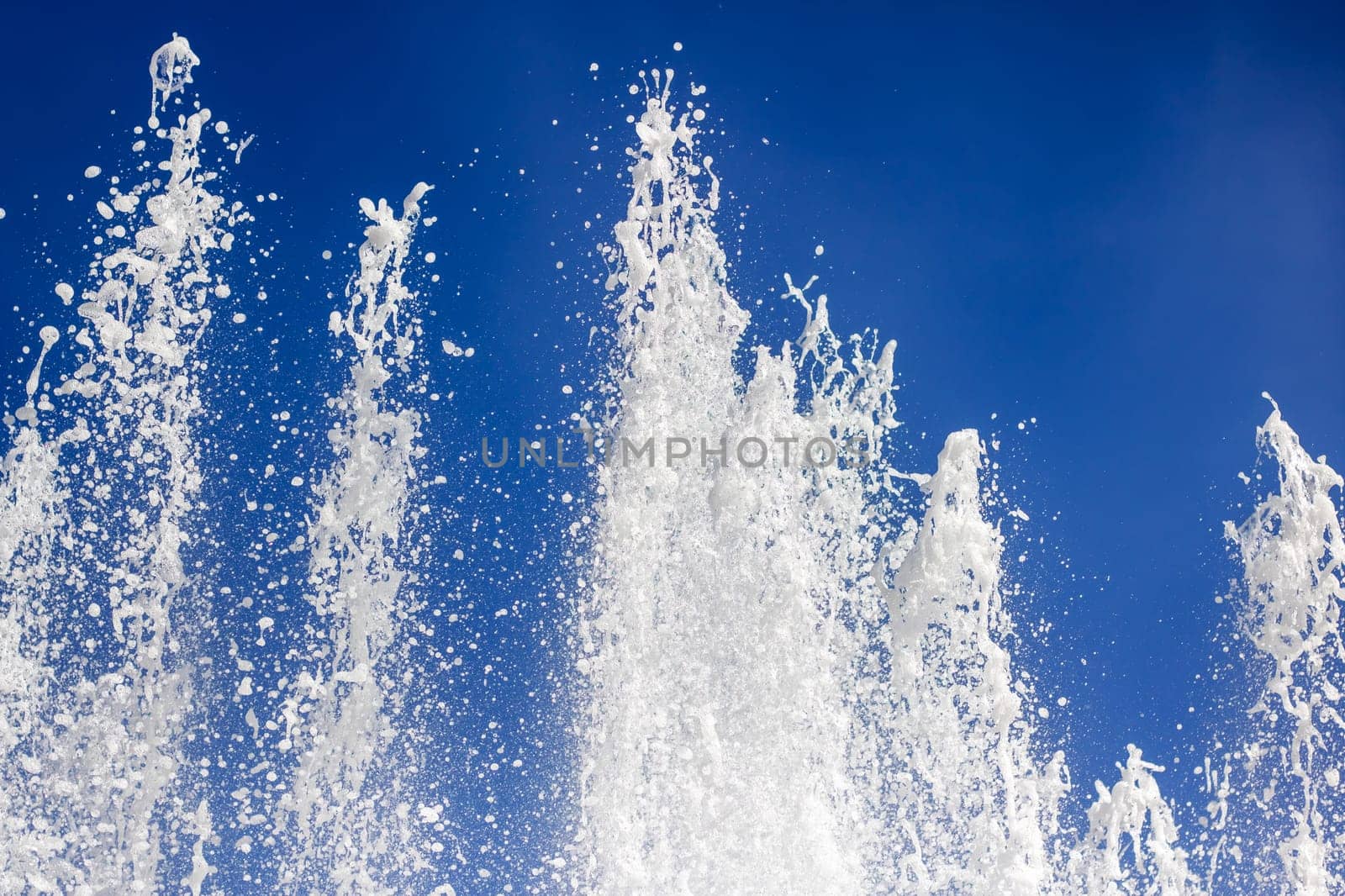 A liquid fountain spraying water against an electric blue sky, creating a stunning natural landscape with trees and clouds in the background