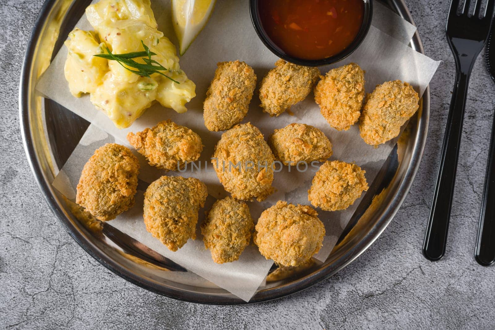 Fried mussels on a metal plate with potato salad on the side. Turkish name: Midye Tava