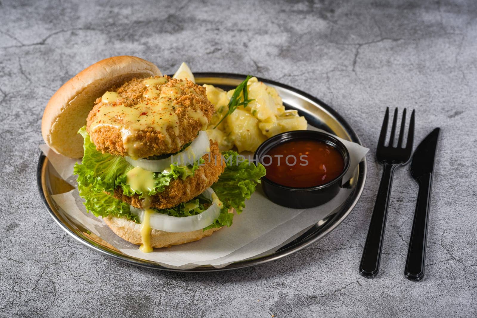 Double fish burger with potato salad on a metal plate by Sonat