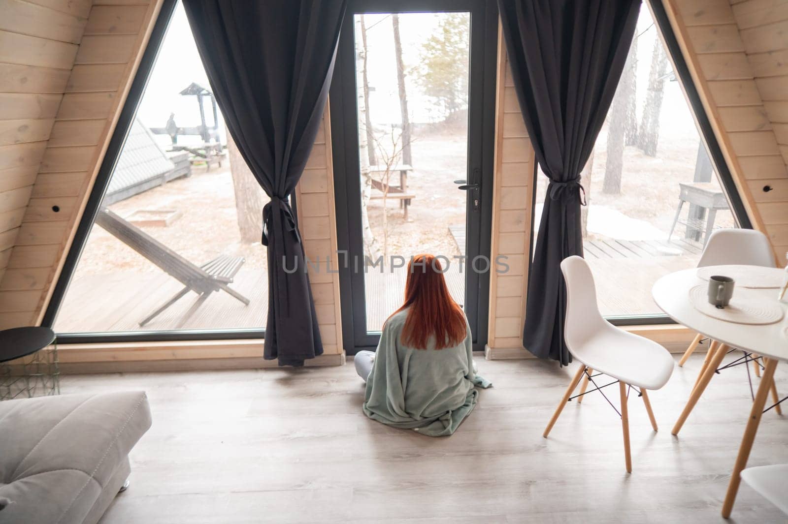Rear view of a red-haired woman wrapped in a blanket looking out the patio window
