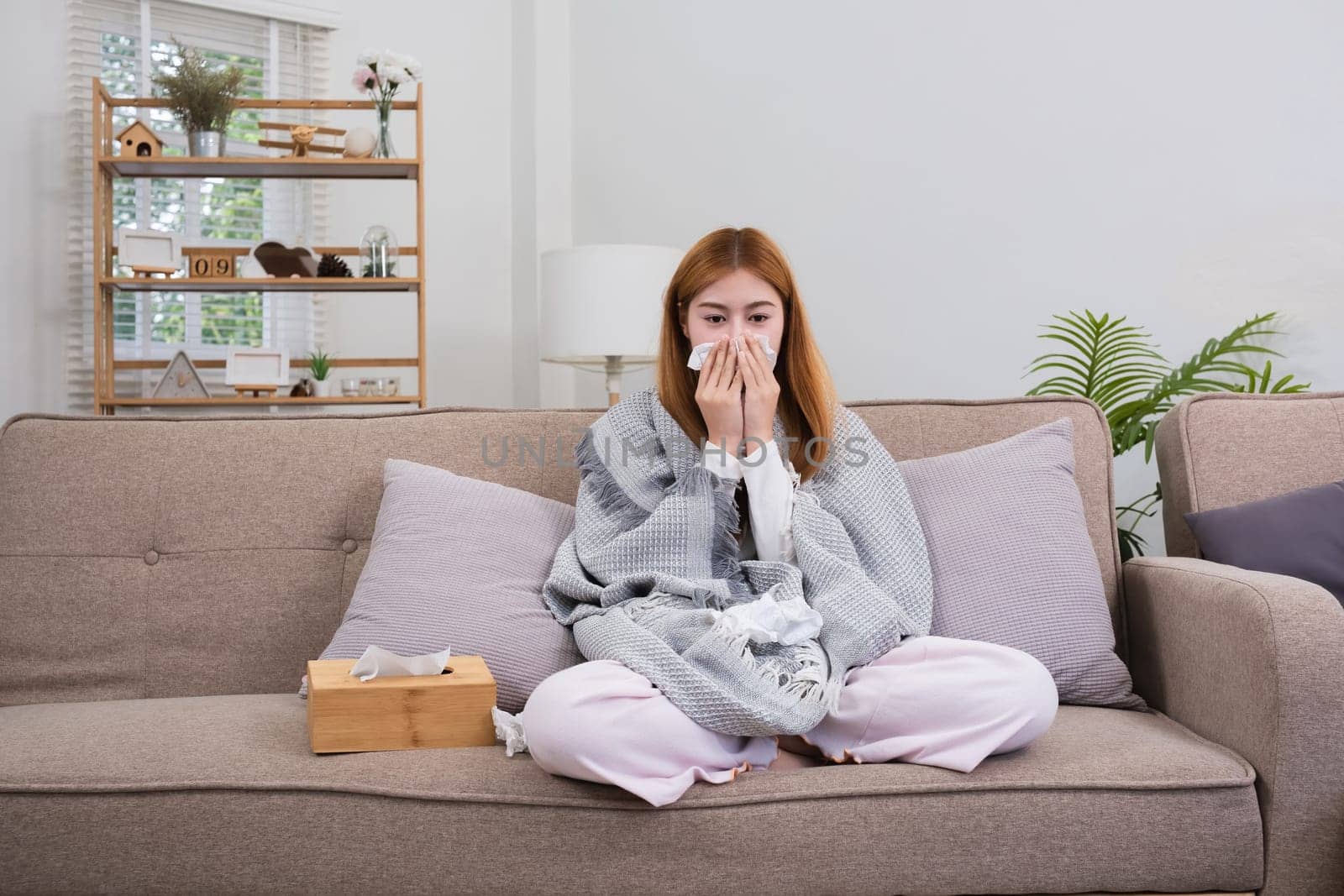 Young Asian woman with cold and allergies feels sick and sneezes on a day of resting at home. by wichayada