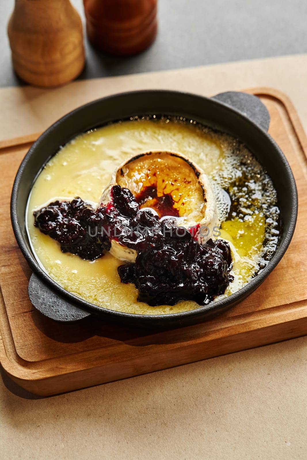 Warm baked Camembert cheese oozing in cast iron skillet served on wooden board, paired perfectly with dollop of homemade currant jam for sweet and savory treat