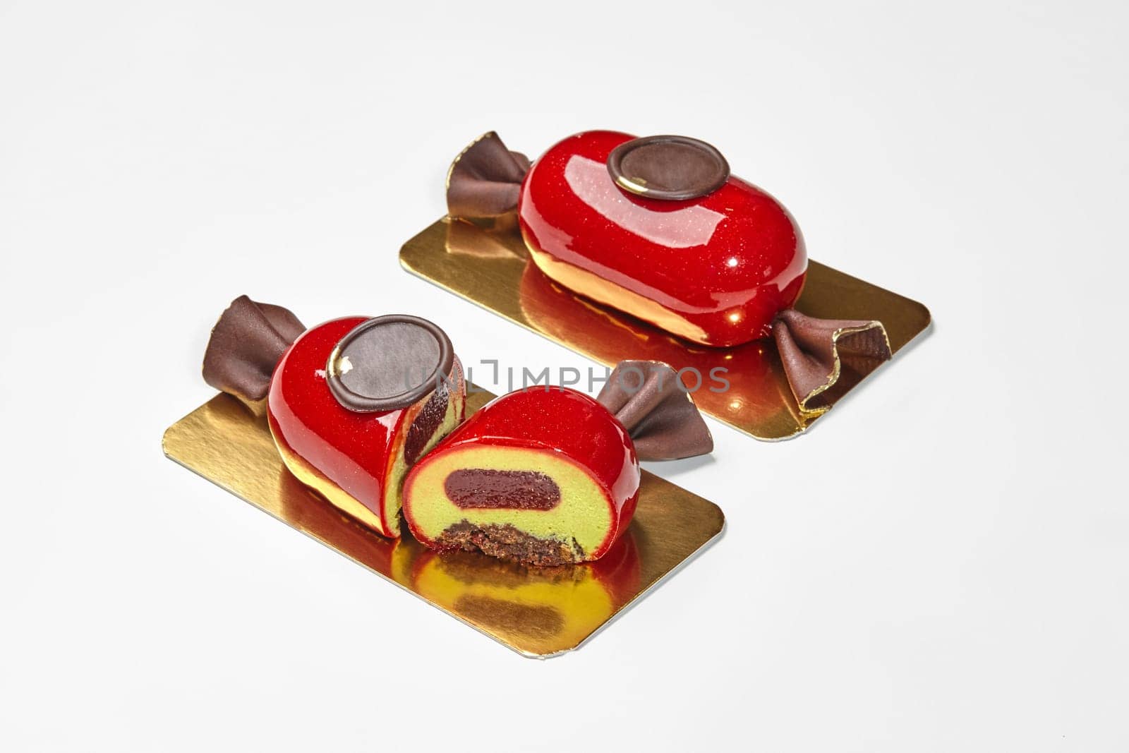 Closeup of sliced artisan candy-shaped dessert with delicate airy vanilla mousse, berry jelly and crispy chocolate streusel decorated with chocolate seal on golden cardboard against white backdrop