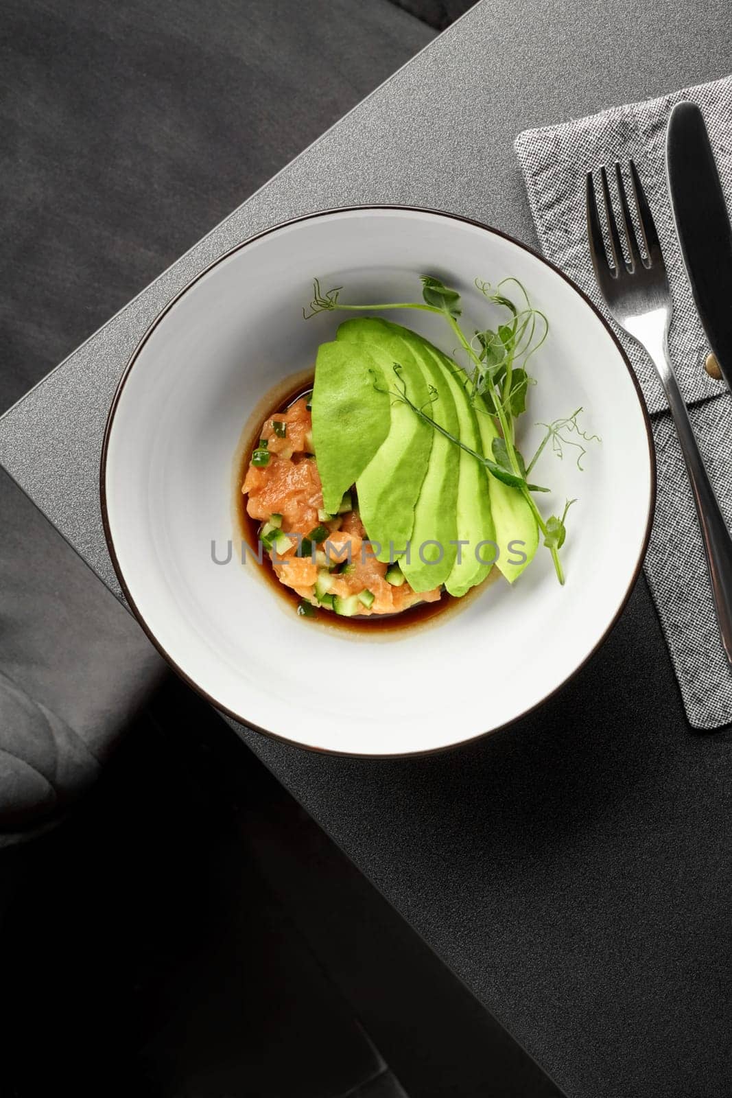 Delicious raw salmon tartare with diced cucumber and ripe avocado slices dressed with flavorful Pan Asian sauce garnished with fresh greens served in white bowl