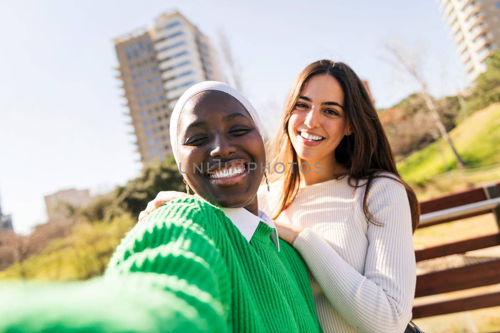 selfie photo of two young female friends smiling happy and having fun in a city park, concept of diversity and modern lifestyle