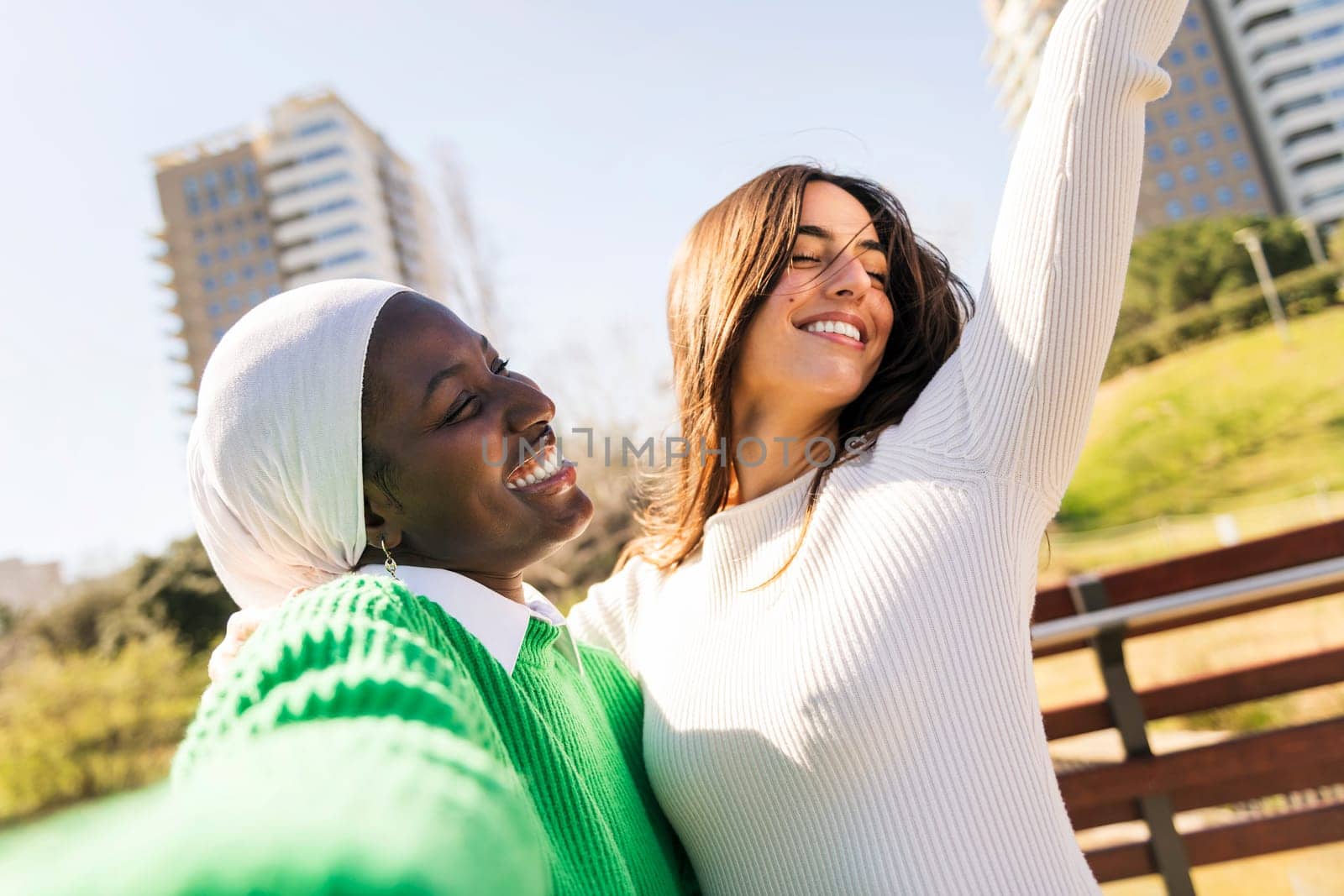 selfie photo of two young female friends laughing carefree and having fun in a city park, concept of diversity and modern lifestyle