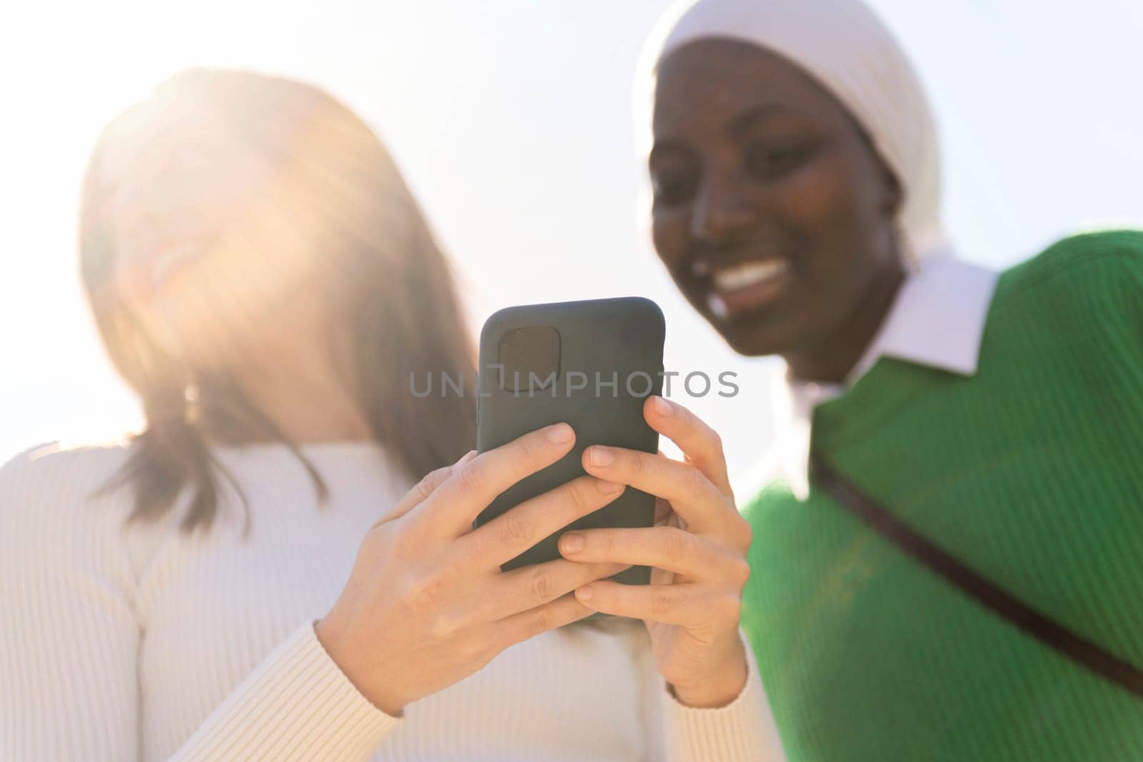 two unrecognizable young women using mobile phone, selective focus on the hands, concept of technology of communication and modern lifestyle