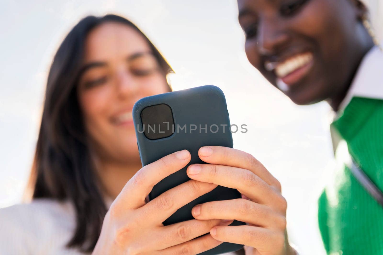 two unrecognizable young women using mobile phone, selective focus on the hands, concept of technology of communication and modern lifestyle