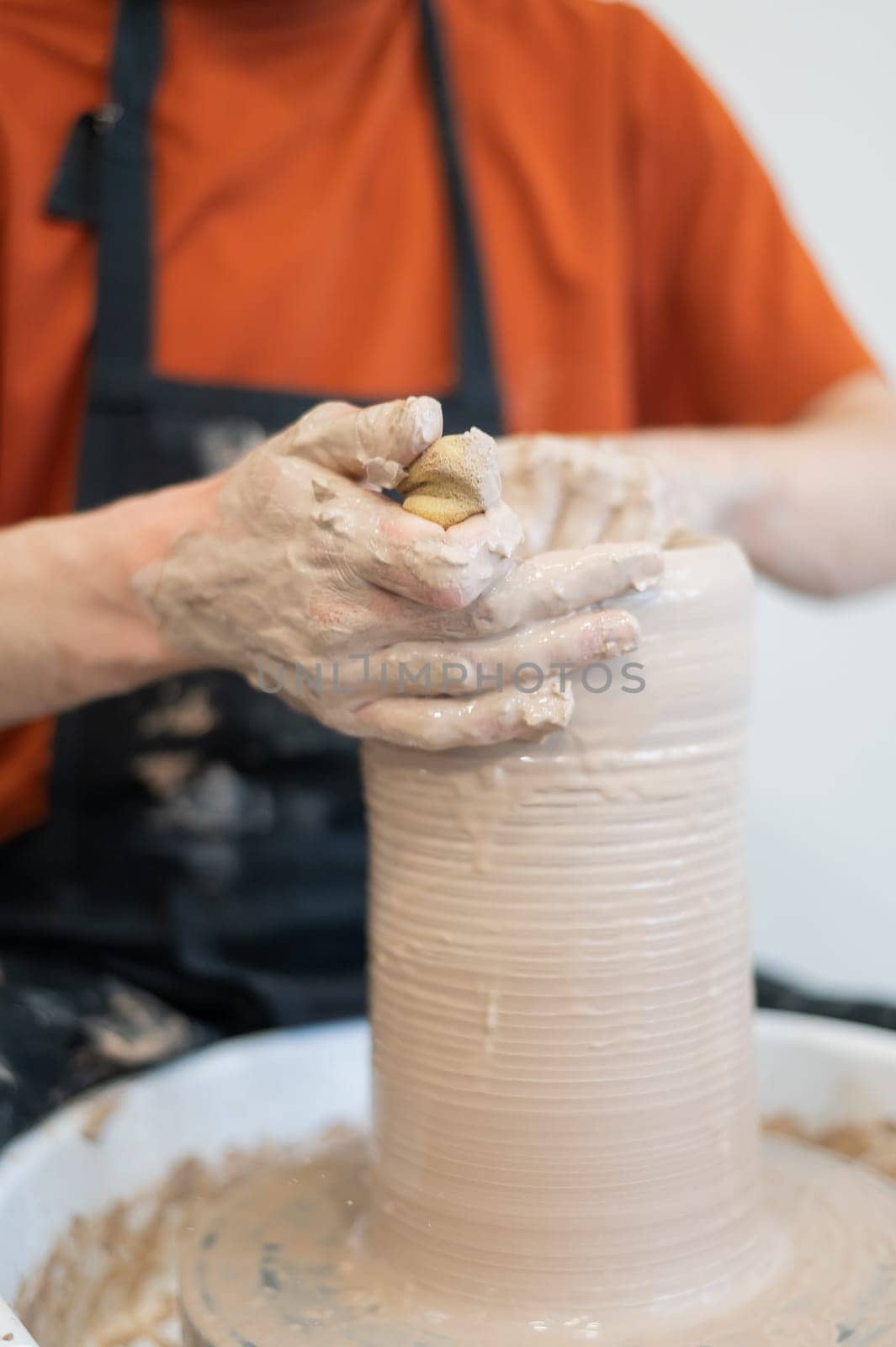 Close-up of a potter's hands making a ceramic vase on a potter's wheel. Vertical photo