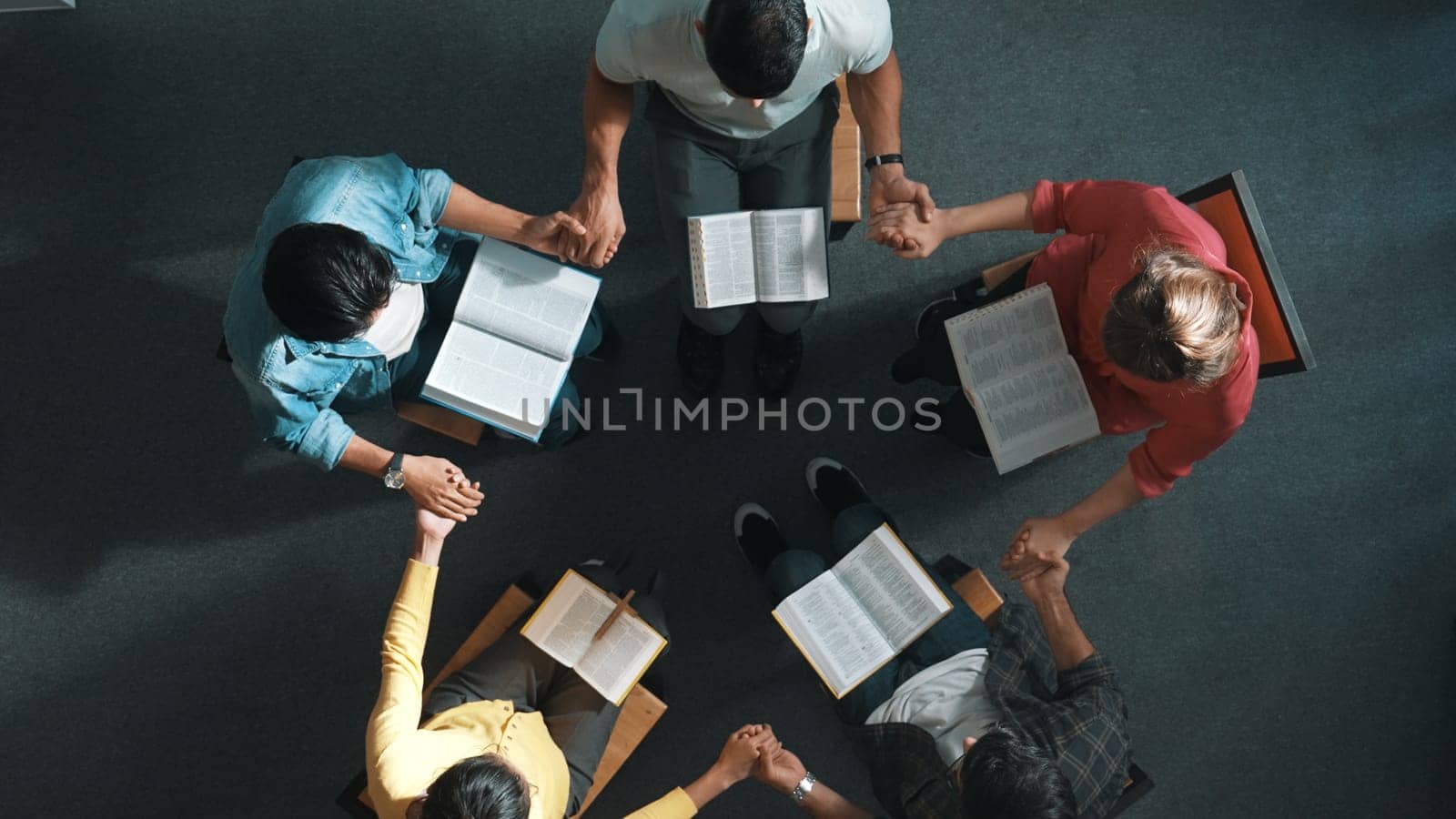 Top down view of diverse people holding hand and sitting in circle with bible book on lap. Aerial view of faithful prayer clasp hand and praying to god with faith, religion conceptional. Symposium.