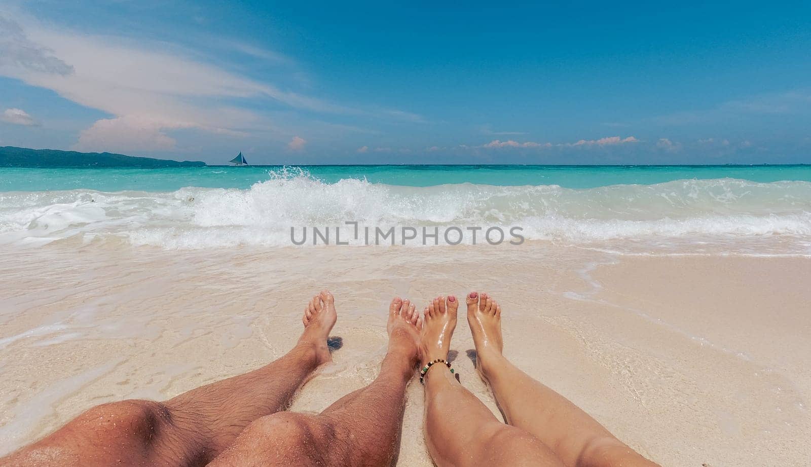 Two people are lying down on the sandy shore of a beautiful beach, enjoying the mid-day sunlight as gentle waves crash nearby. Boracay, Philippines.