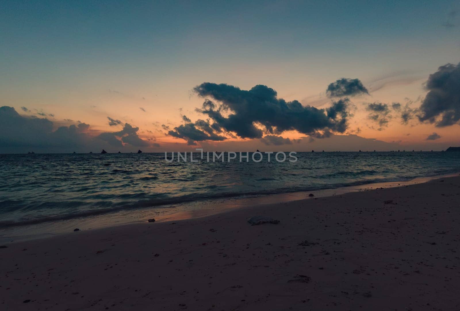 Calm evening on a sandy beach with boats sailing in the distance. Boracay, Philippines. by Busker