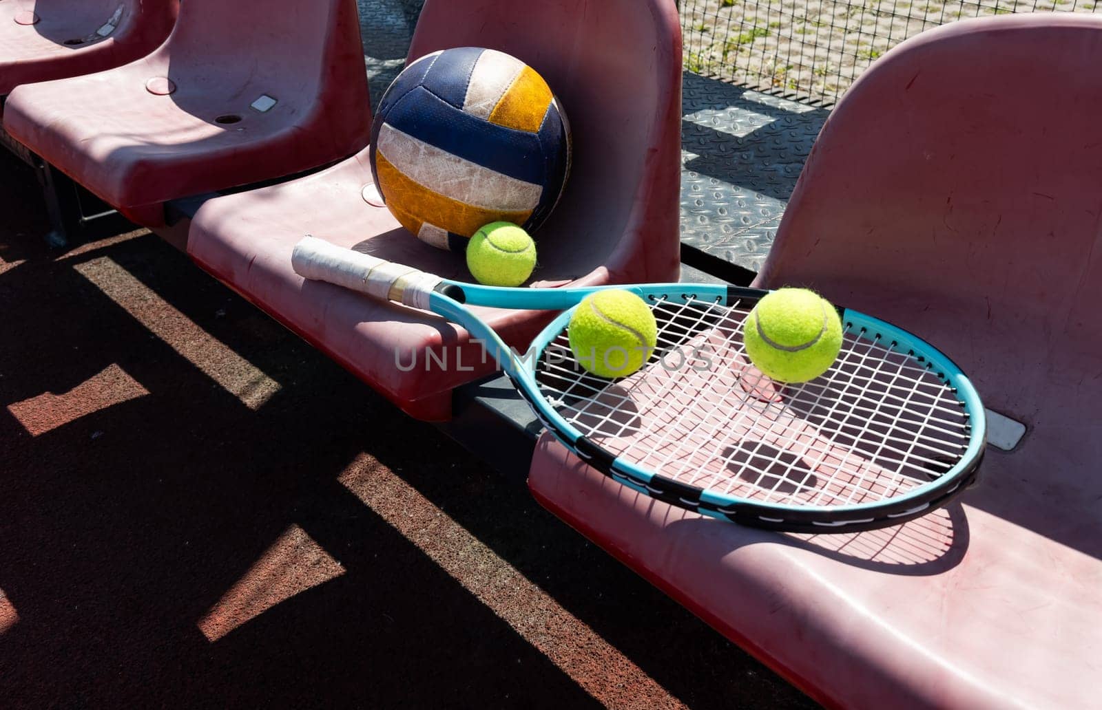 a tennis racket, balls and a volleyball on a bench on the sports tribune. High quality photo