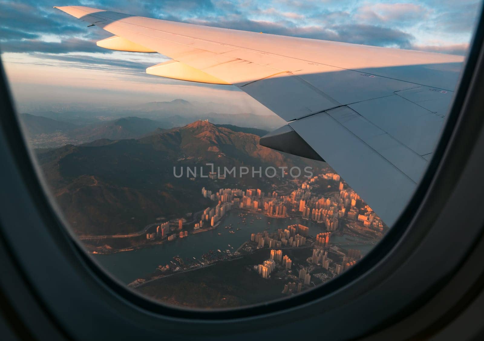 Aerial view of Hong Kong city buildings and river at sunset from airplane window
