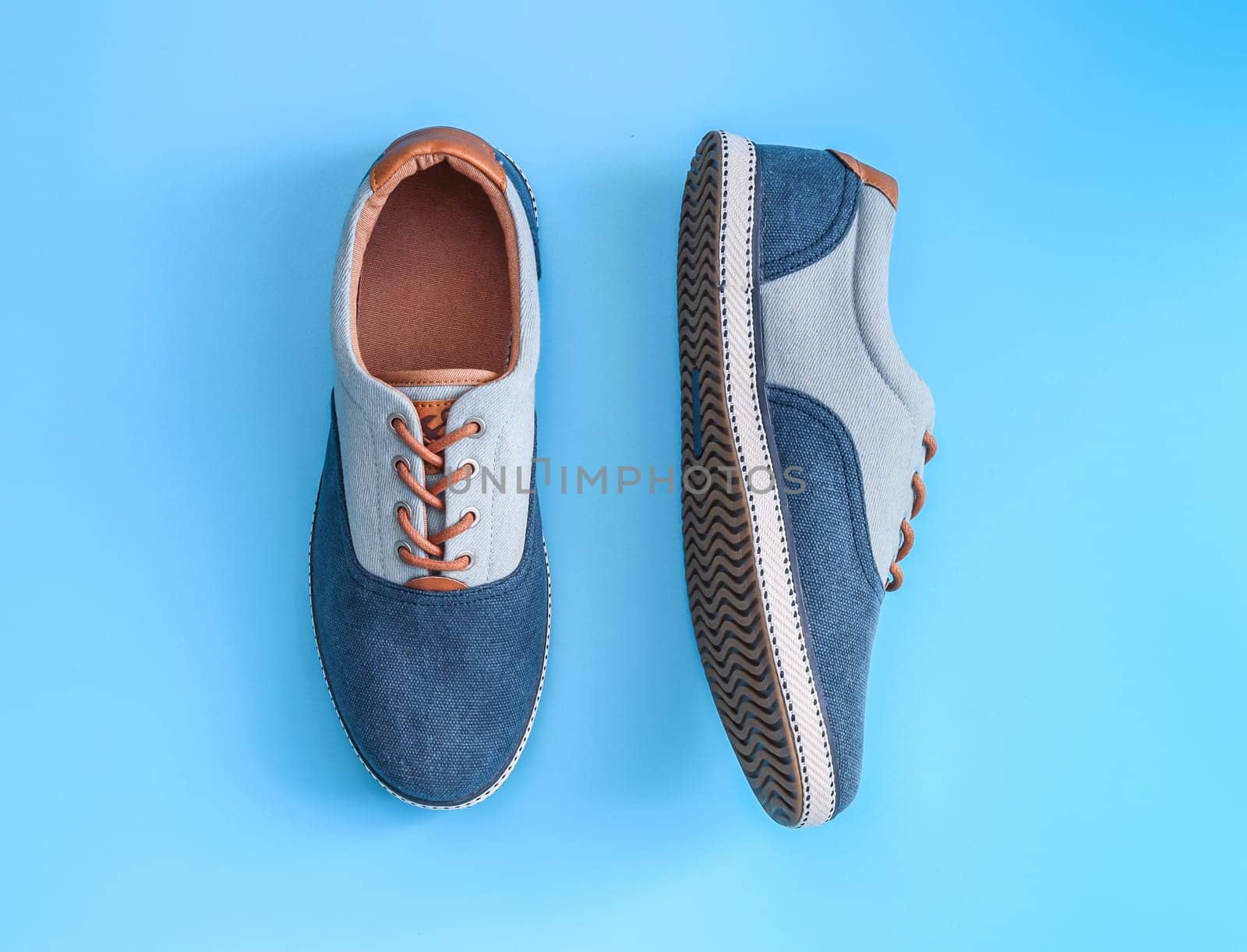 One pair of denim sneakers lies in the center on a blue background, flat lay close-up. The concept of fashion, beauty, man shoes.