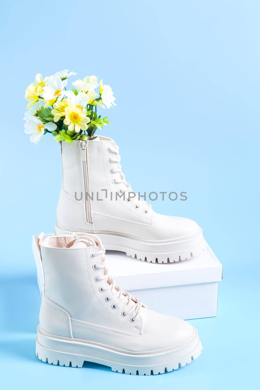 White demi-season martens boots made of eco-leather with a rough sole with a bouquet of spring flowers and a white cardboard box for shoes stand on a light blue background, close-up side view. The concept of women's shoes.