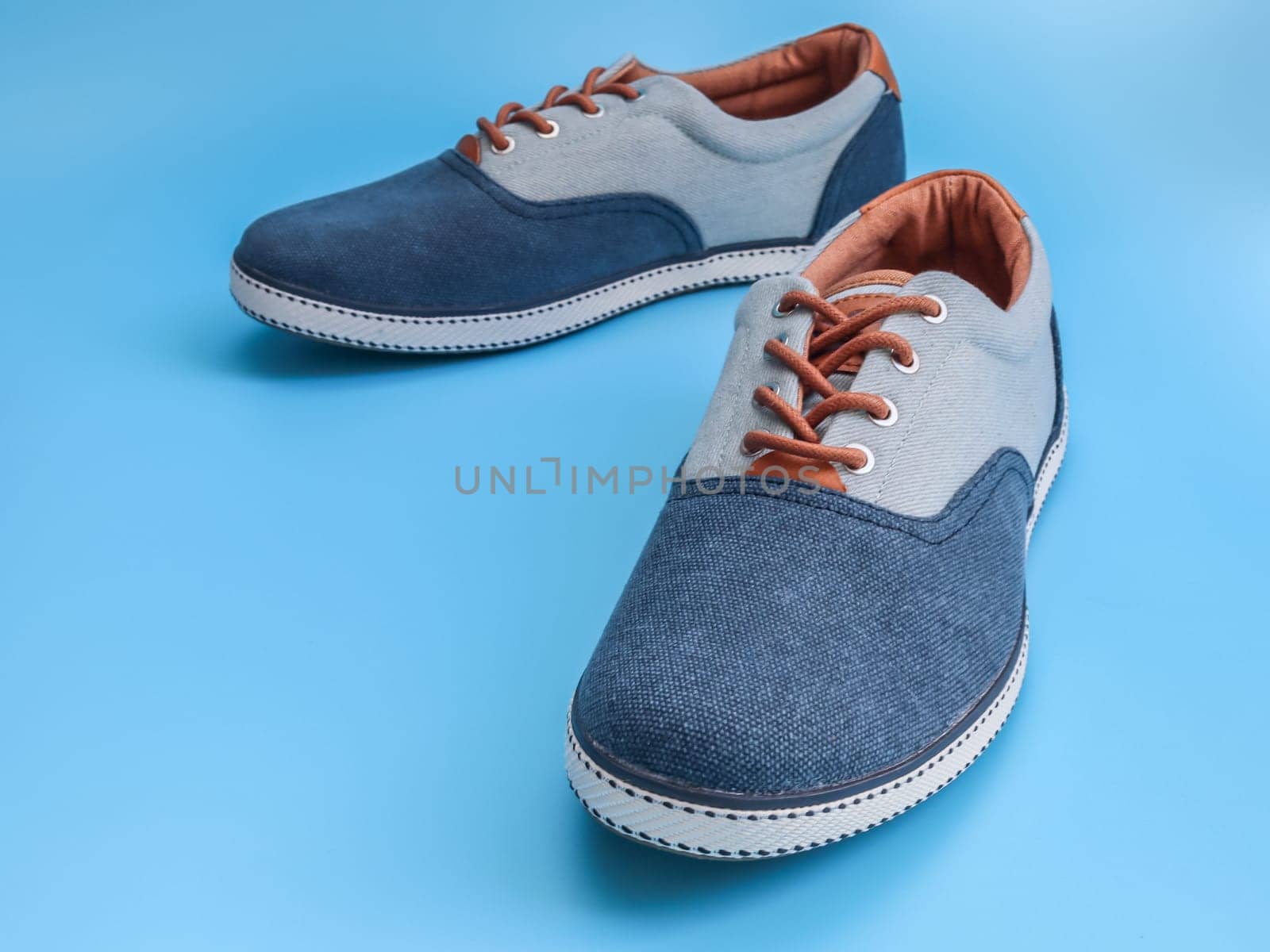 One pair of denim sneakers lies in the center on a blue background, close-up side view. The concept of fashion, beauty, man shoes.