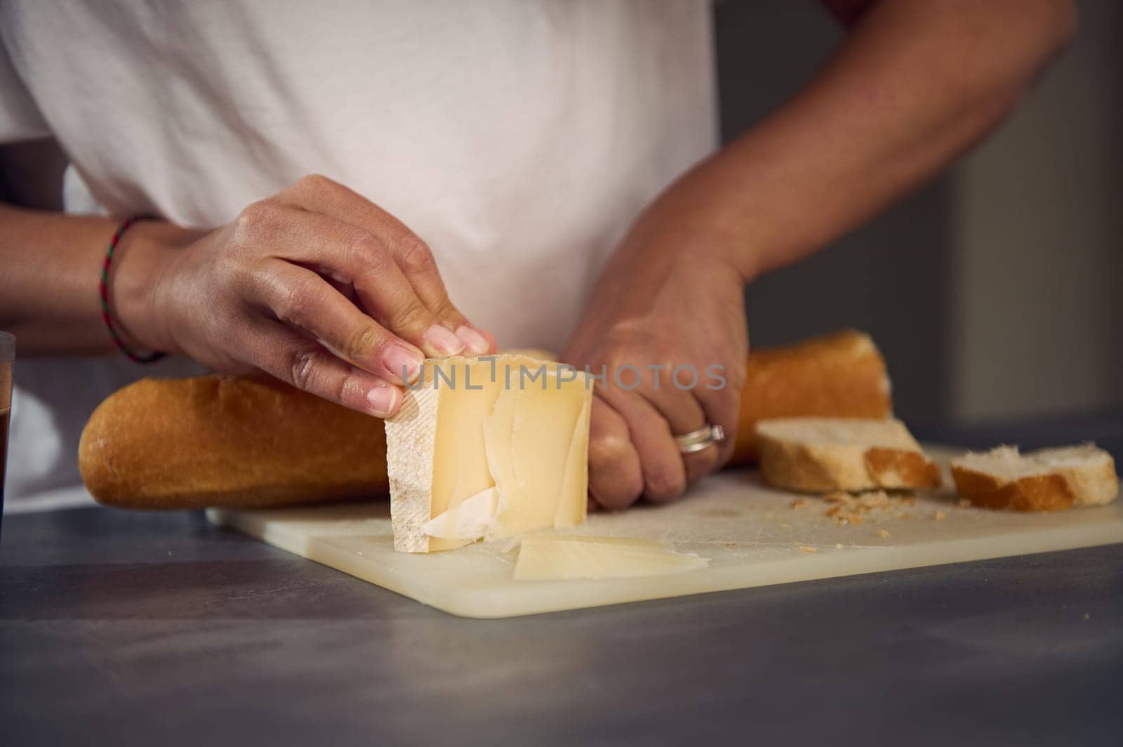 Close-up hands of a woman slicing cheese on cutting board, using a kitchen knife, preparing sandwiches for a healthy breakfast.