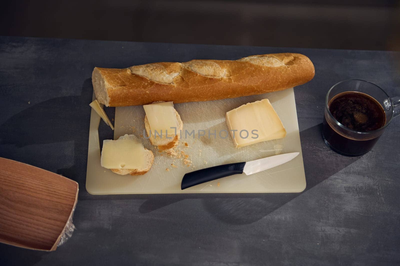 Still life top view breakfast on the kitchen table. A cup of freshly brewed espresso coffee near a cutting board with a whole grain baguette, loaf of bread and sliced cheese on the kitchen table