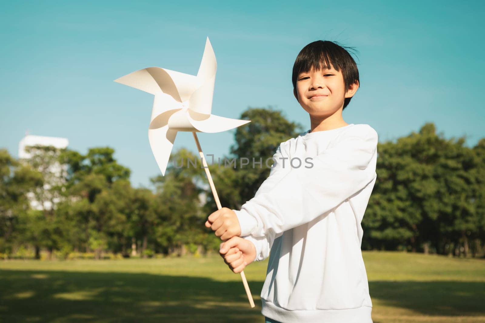 Little asian boy holding windmill or wind turbine mockup model to promote eco clean and renewable energy technology utilization for future generation and sustainable Earth. Gyre