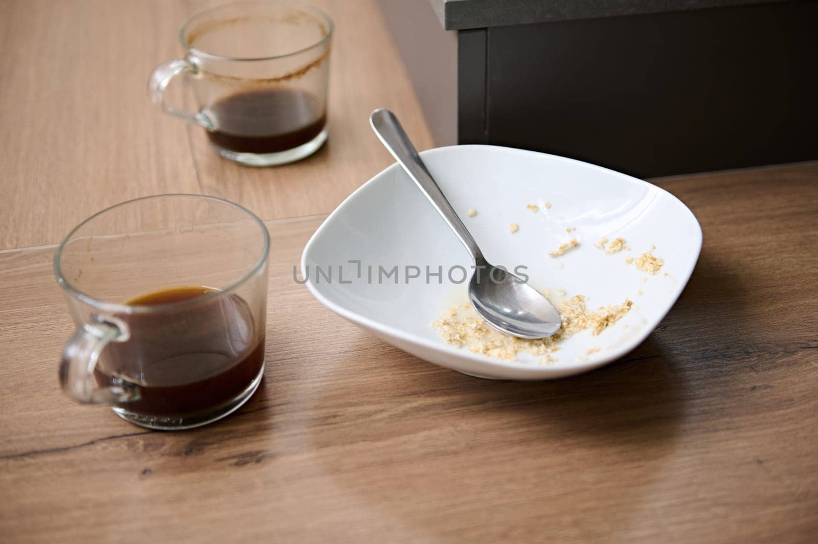 View from above of left over of breakfast in white ceramic bowl and two glass cups of unfinished coffee on the table