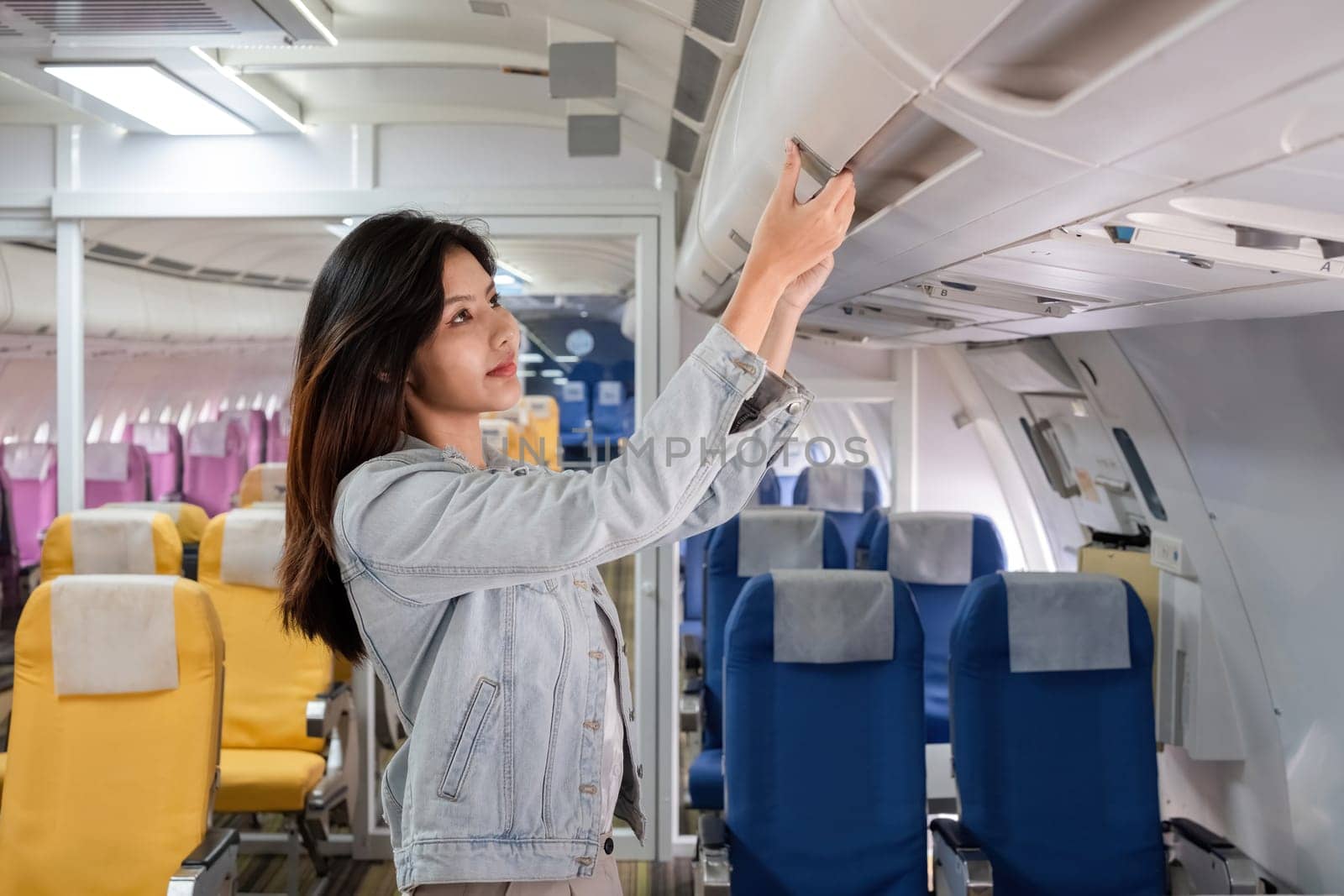 Asian woman adjusting overhead bin in airplane cabin. Concept of travel, aviation, and in-flight preparation by wichayada