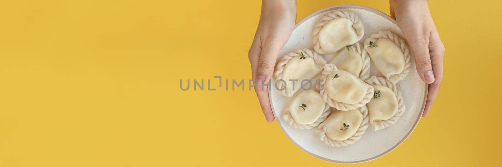 Banner of female hands holding plate of ravioli or dumplings. top view of plate on yellow background by Leoschka