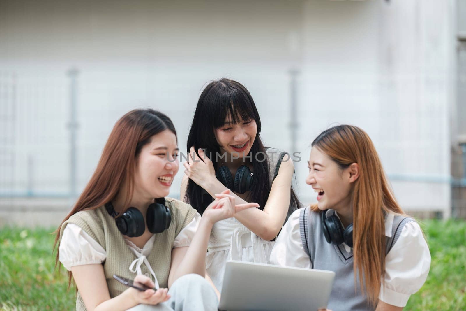 Group of young university students laughing and studying on campus lawn. Friends enjoying outdoor learning and bonding. Concept of education, friendship, and student life.