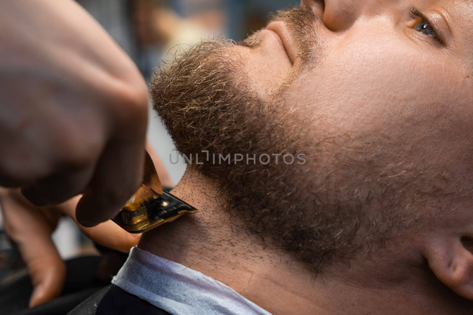 Master barber employs an automatic trimmer to groom the clients beard at the barbershop.