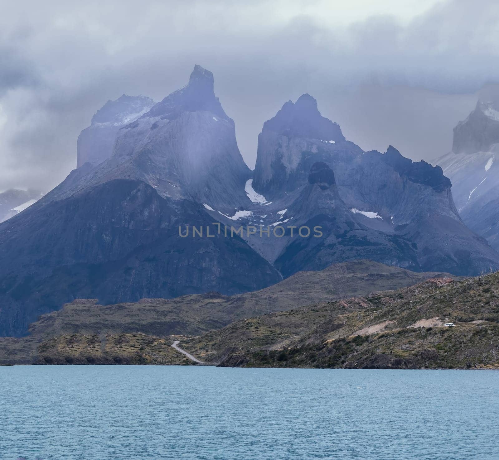 Dramatic mountains rise above a calm turquoise lake under moody skies.