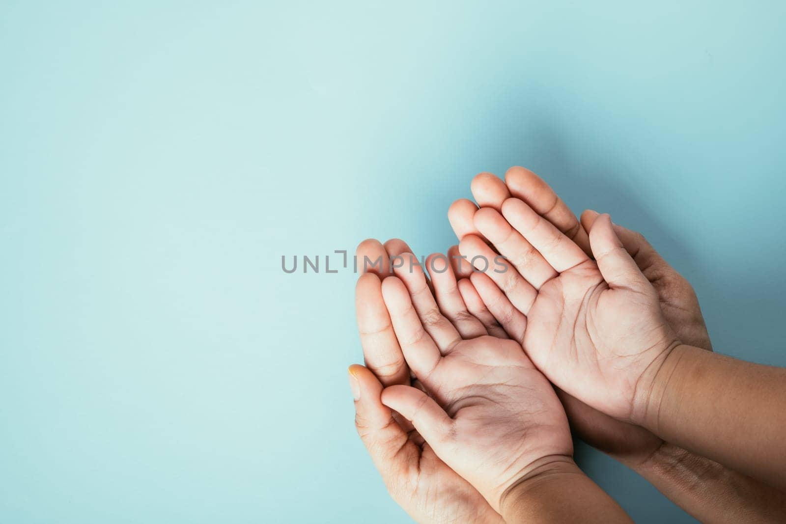 Studio shot, Close-up top view family hands stacked on an isolated background. Parents and kid hold empty space together symbolizing support and love for Family and Parents Day.