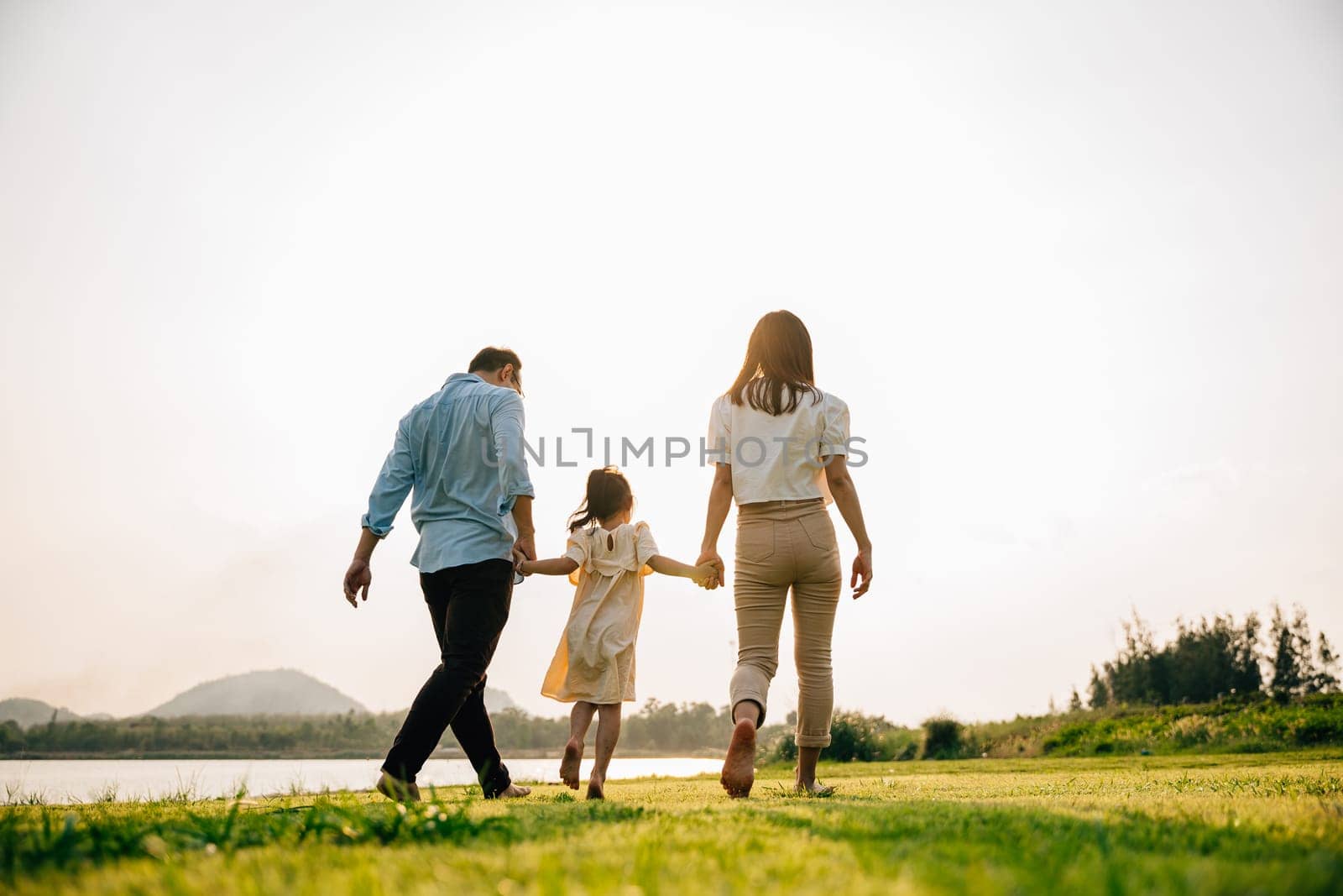 Happy Asian family walking and playing together in a beautiful nature setting, with green grass and a sunny background, on a summer day, Family day, back view