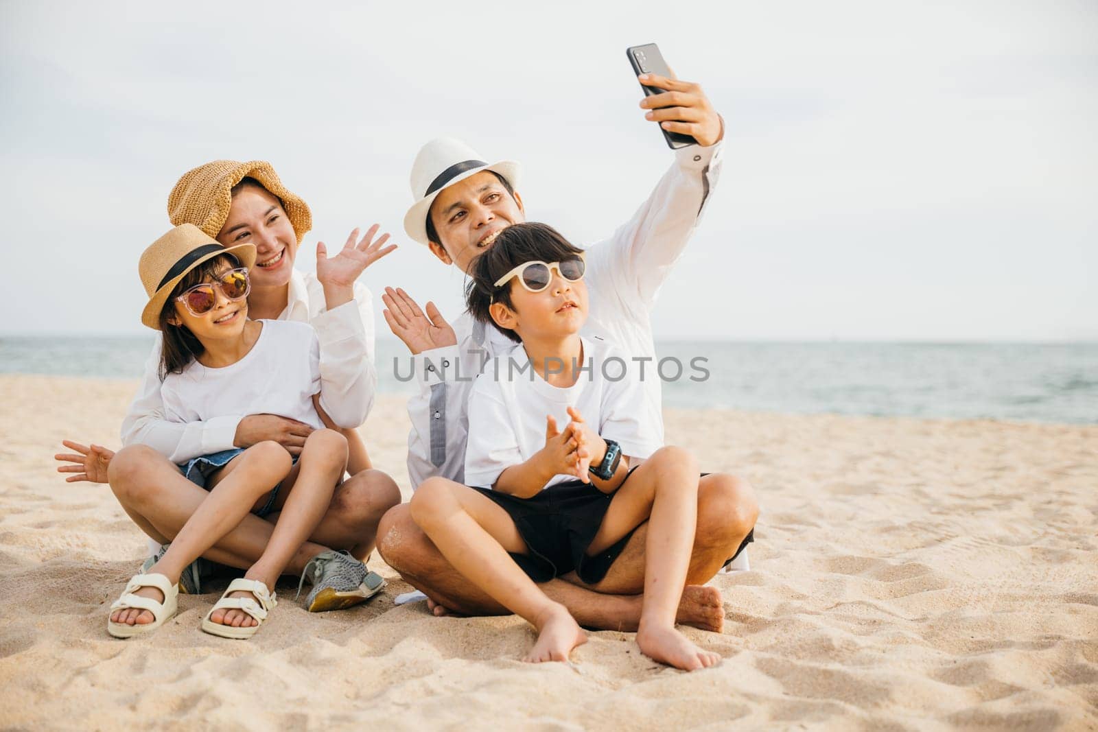 Summer joy on display as a happy family takes a lively selfie on the beach near the sea. Laughter smiles and the warmth of togetherness make this portrait a perfect capture of family happiness. by Sorapop