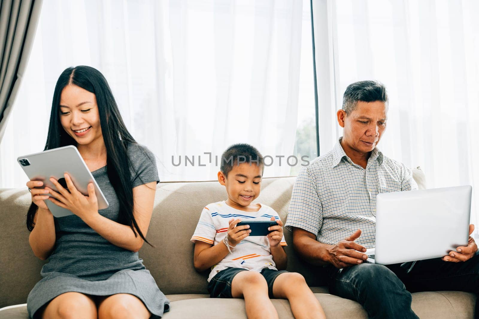 An Asian family engrossed in devices at home neglects bonding time by Sorapop