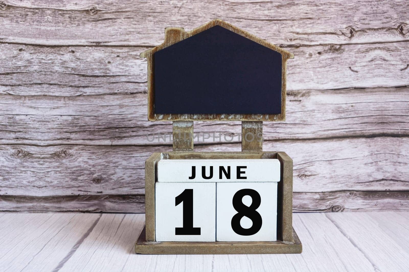 Chalkboard with June 18 calendar date on white cube block on wooden table.