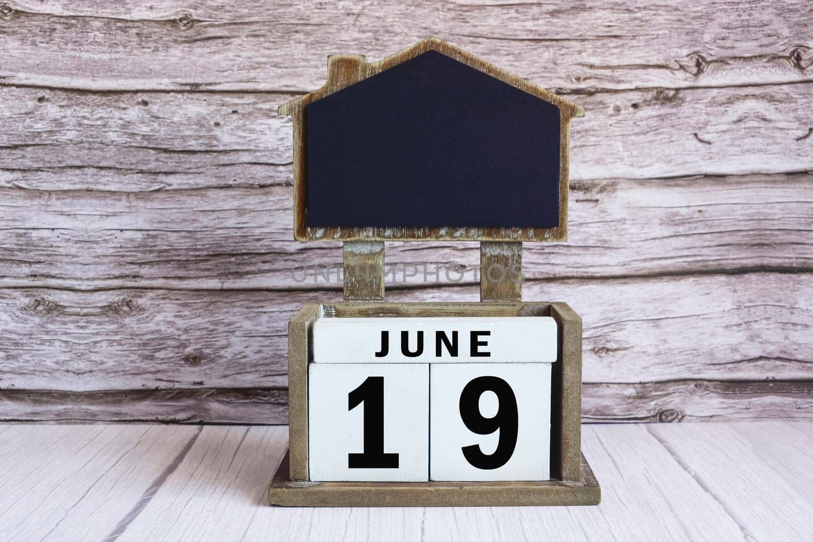 Chalkboard with June 19 calendar date on white cube block on wooden table.