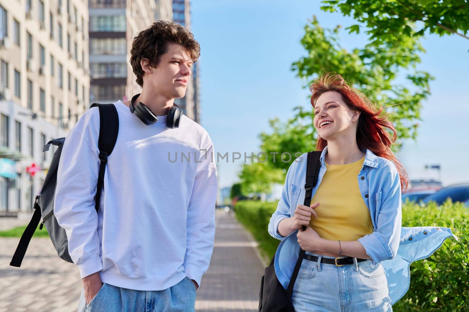 Talking walking friends, guy and girl, university college students walking together along street of modern city. Youth 19-20 years old, friendship, communication, urban lifestyle concept