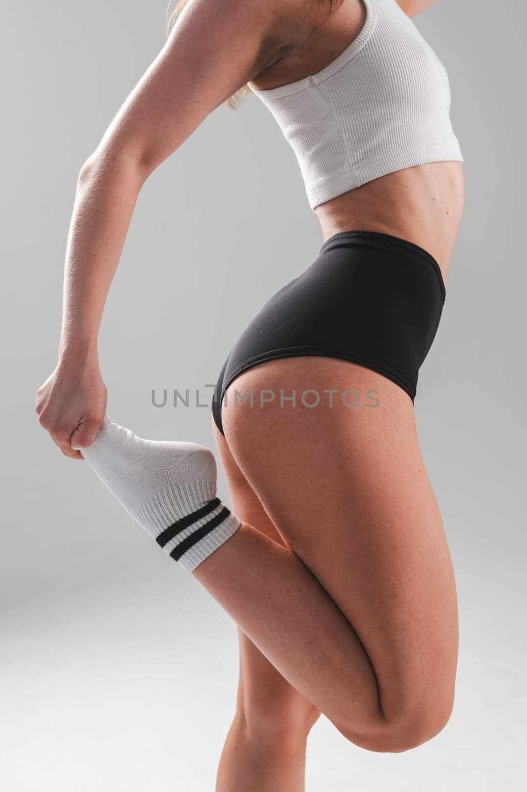 Faceless woman stretching her quadriceps on a white background. Vertical photo. by mrwed54