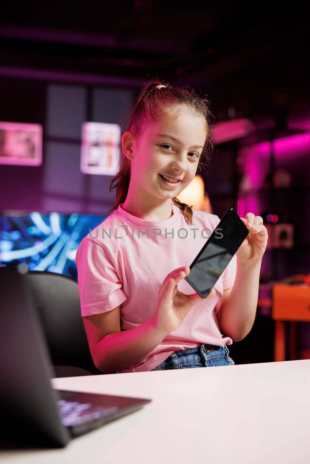 Kid internet show host filming content about best cellphones on the market in neon pink lit apartment. Young media star recording mobile phone review for tech enthusiasts