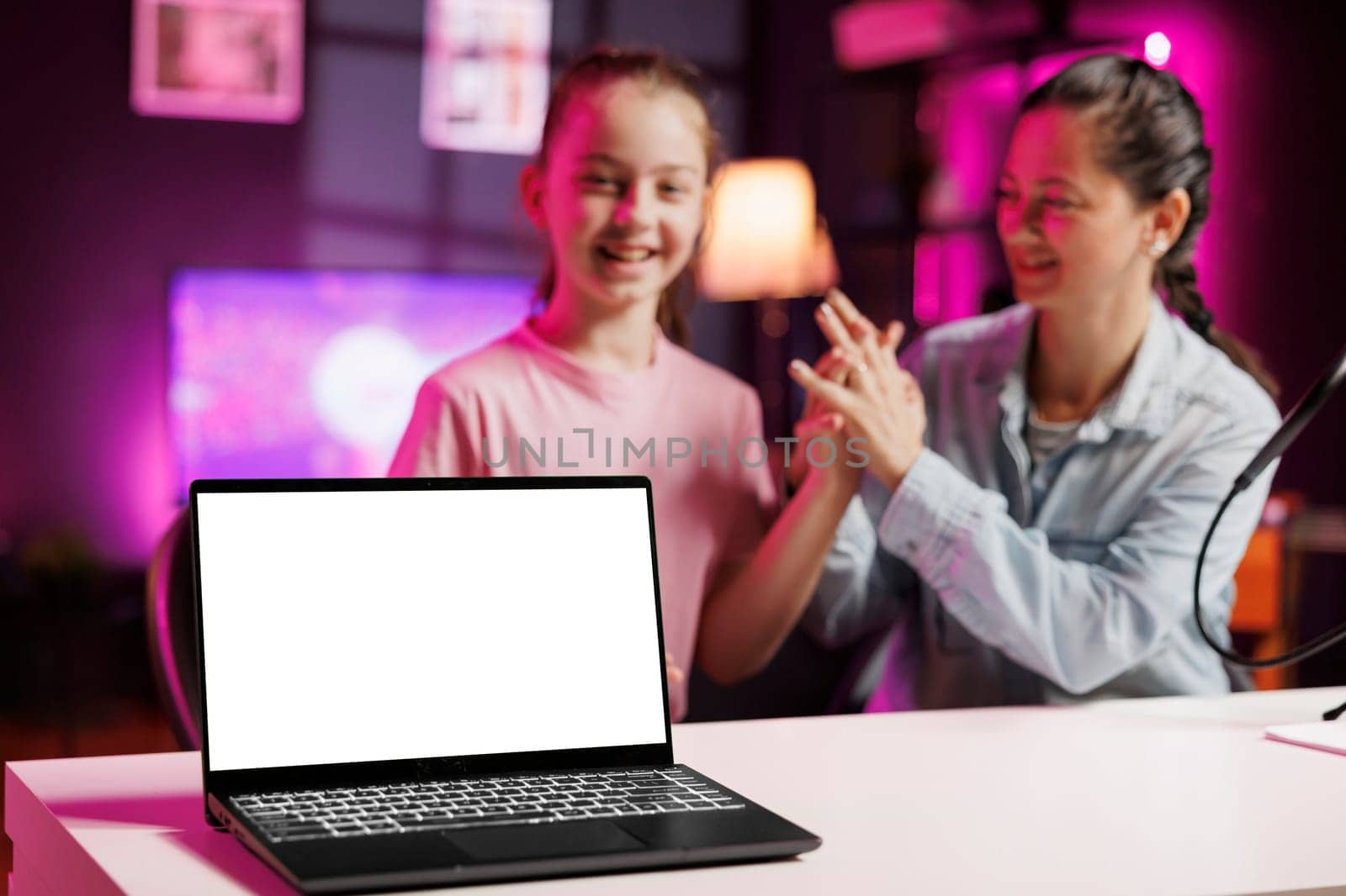 Cheerful girl next to her mother presents mockup laptop in pink neon lit living room by DCStudio