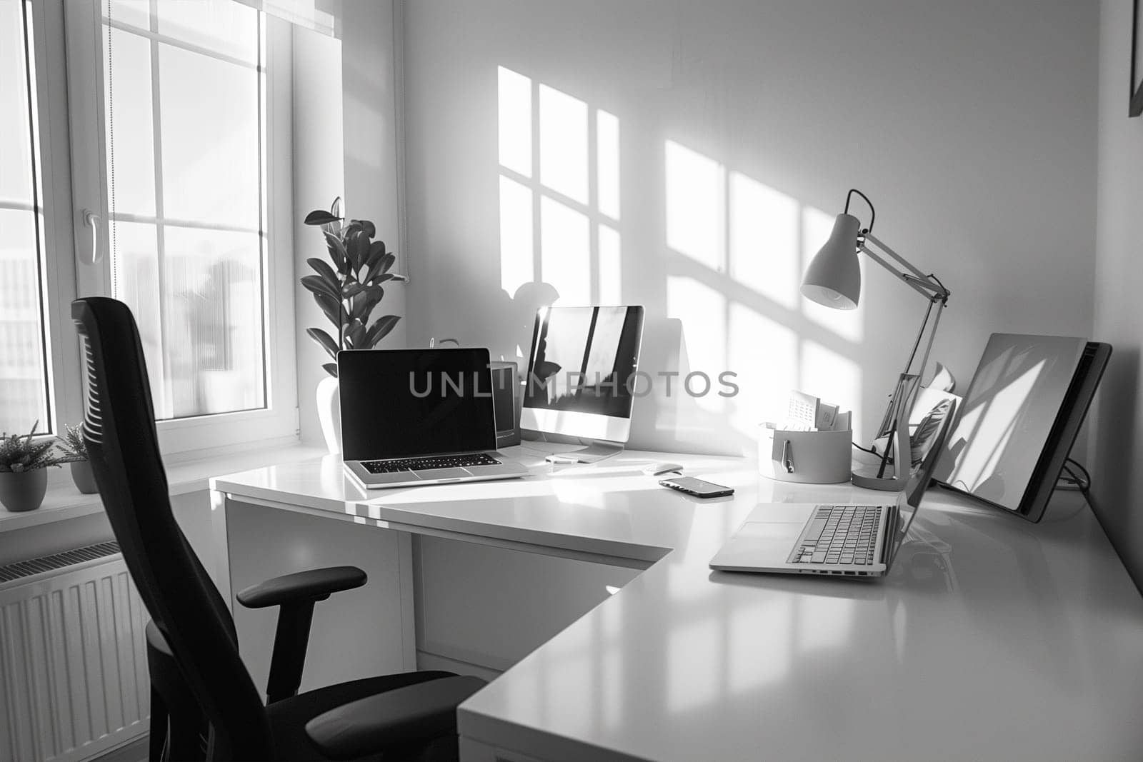 A monochromatic photo featuring a desk with a laptop placed on it.