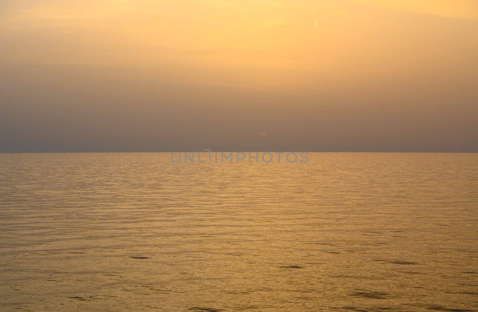 sun sets on a dramatic cloudy sky over the Mediterranean Sea horizon with a warm, golden glow.