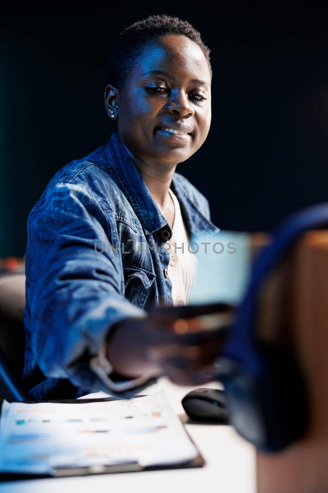 Image showing blue sticky note and wireless headphones placed on wooden stand by african american female influencer. Close-up shot of black woman putting a written paper on board as a reminder.