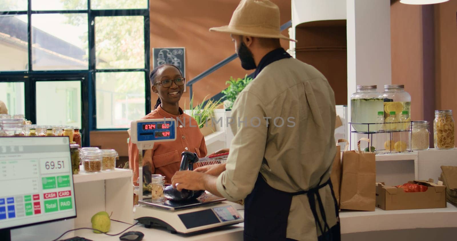 Seller weighting produce for woman, placing fruits and veggies on scale to ensure right price at local zero waste supermarket. Small business owner serving young client with groceries.