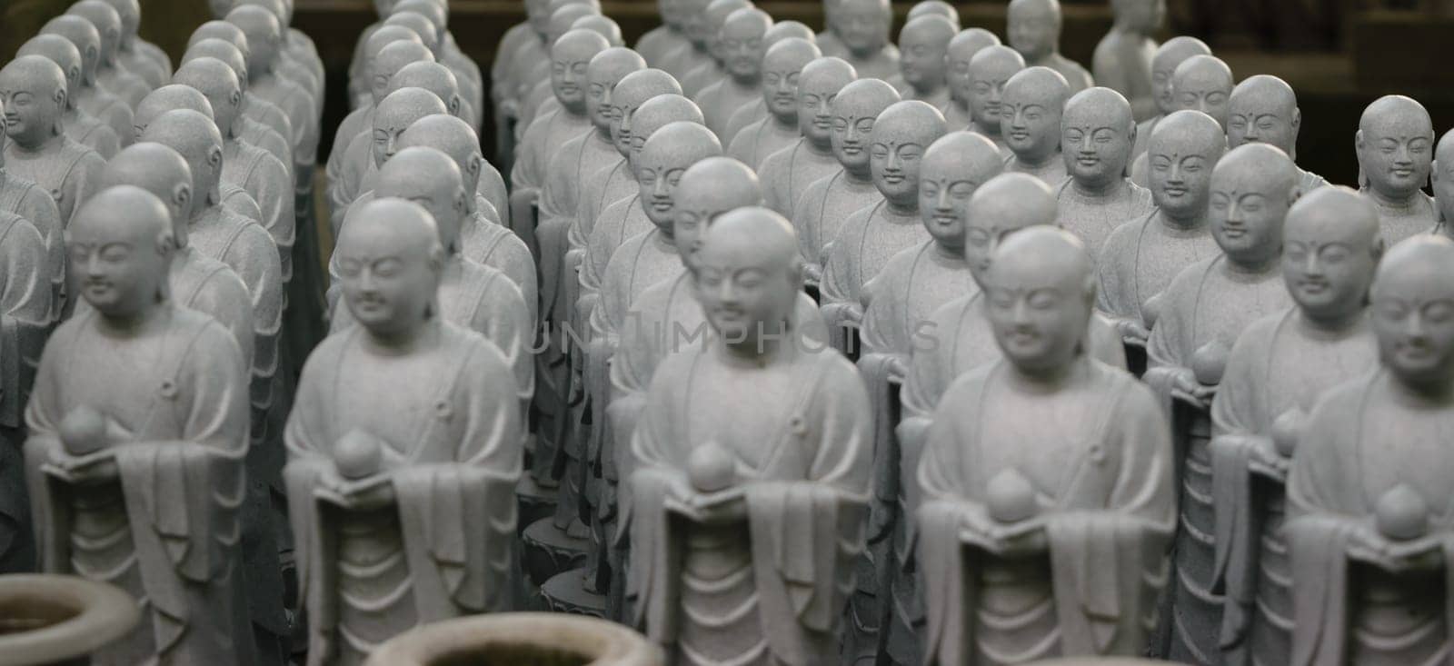 A collection of small, identical stone Buddha statues arranged in rows. Each statue is holding a small object and has a serene expression.