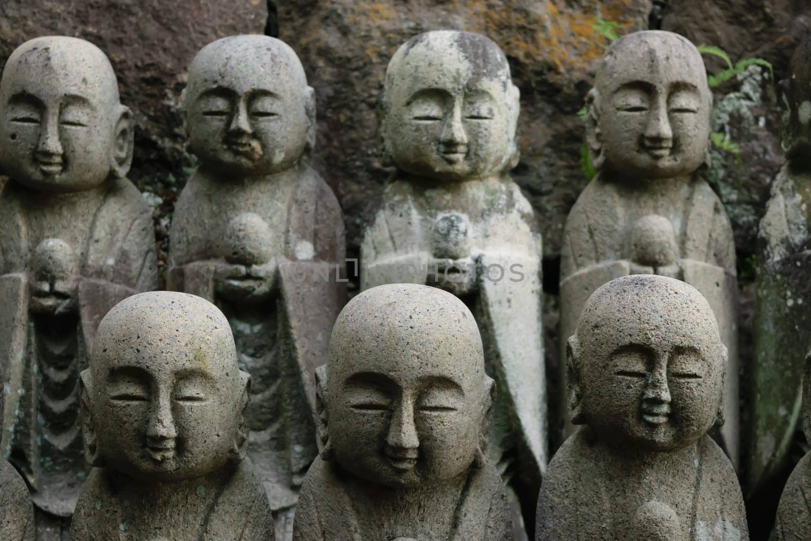 A close-up of multiple stone Buddha statues arranged in rows, with moss and weathering visible on some of them. The statues have serene expressions and are set against a rocky background.